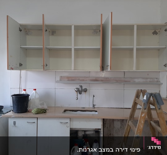 מוצרי ניקוי ודלי במטבח עם ארונות פתוחים